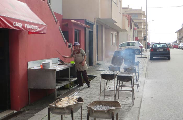 Una mujer atiende las parrillas donde se cocina el pescado fresco comer en Furadouro